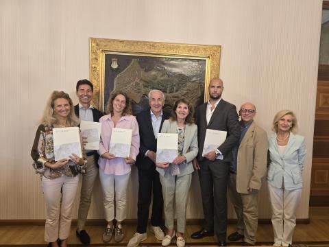 Costituita la rete d'impresa delle “Dimore Storiche della Contea di Gorizia” Otto persone in posa con cartelle davanti a una mappa del Comune di Gorizia.