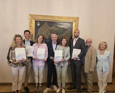 Otto persone in posa con cartelle davanti a una mappa del Comune di Gorizia.